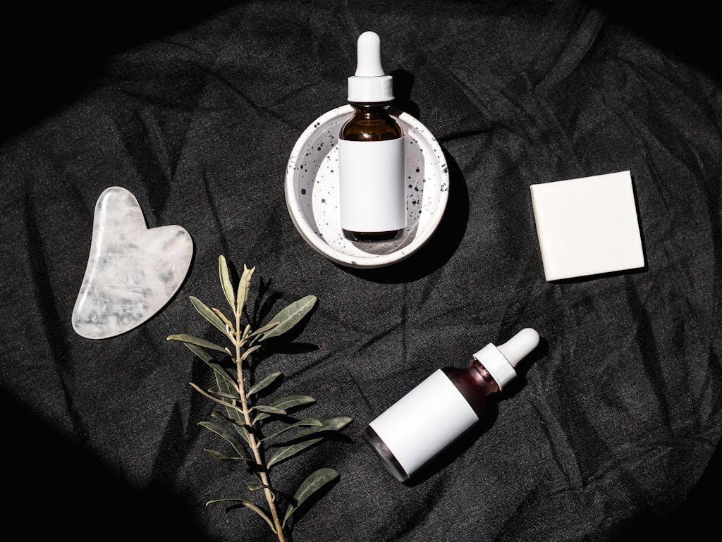 Brown Glass Bottles on Black Textile Beside Gua Sha and Leaves