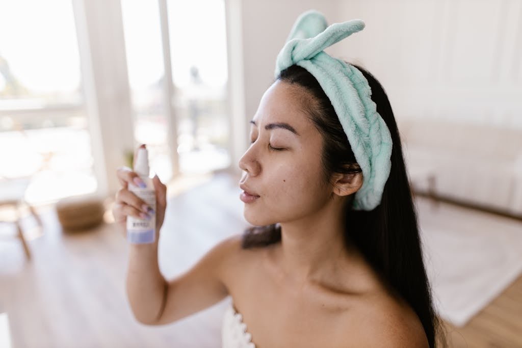 Woman Sitting in a Towel and with a Hair Band on Her Head Spraying Her Face with a Mist